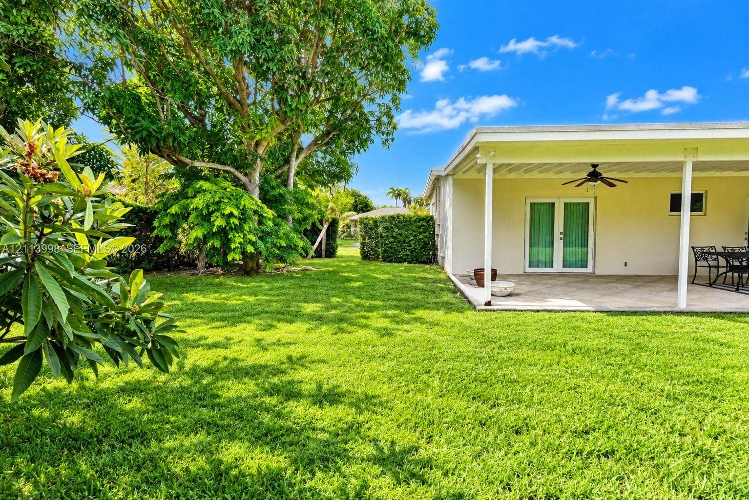 16455 SW 91st Avenue, Palmetto Bay, FL 33157 Expansive backyard featuring a manicured lawn, mature trees, and a covered patio with a ceiling fan