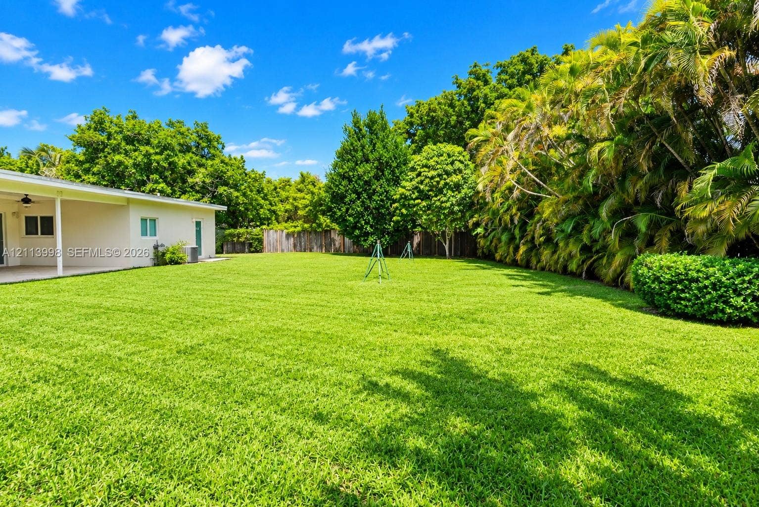 16455 SW 91st Avenue, Palmetto Bay, FL 33157 Expansive backyard featuring a large grass lawn, covered patio, mature perimeter landscaping, and wooden privacy fencing