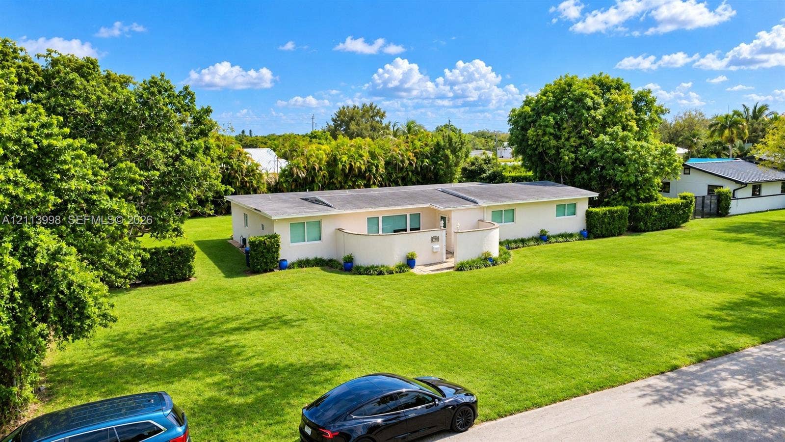 16455 SW 91st Avenue, Palmetto Bay, FL 33157 Single-story exterior featuring a curved masonry privacy wall, a low-pitch roofline, and an expansive lawn with mature perimeter landscaping