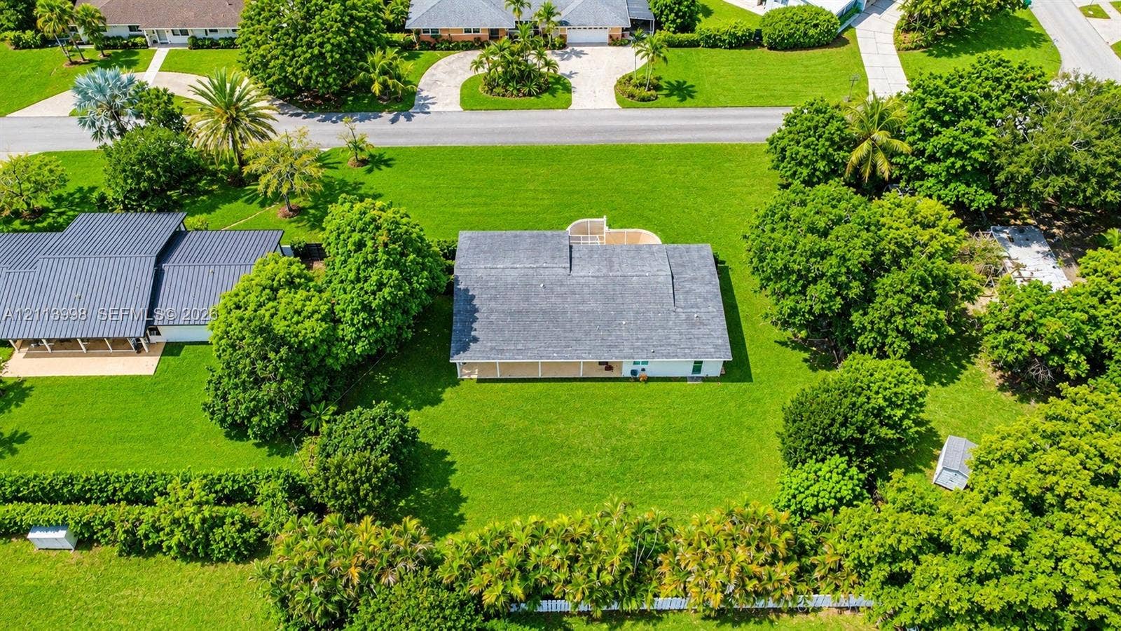 16455 SW 91st Avenue, Palmetto Bay, FL 33157 Aerial perspective featuring a single-story residence with a shingle roof, integrated rear covered patio, expansive manicured lawn, and mature perimeter landscaping