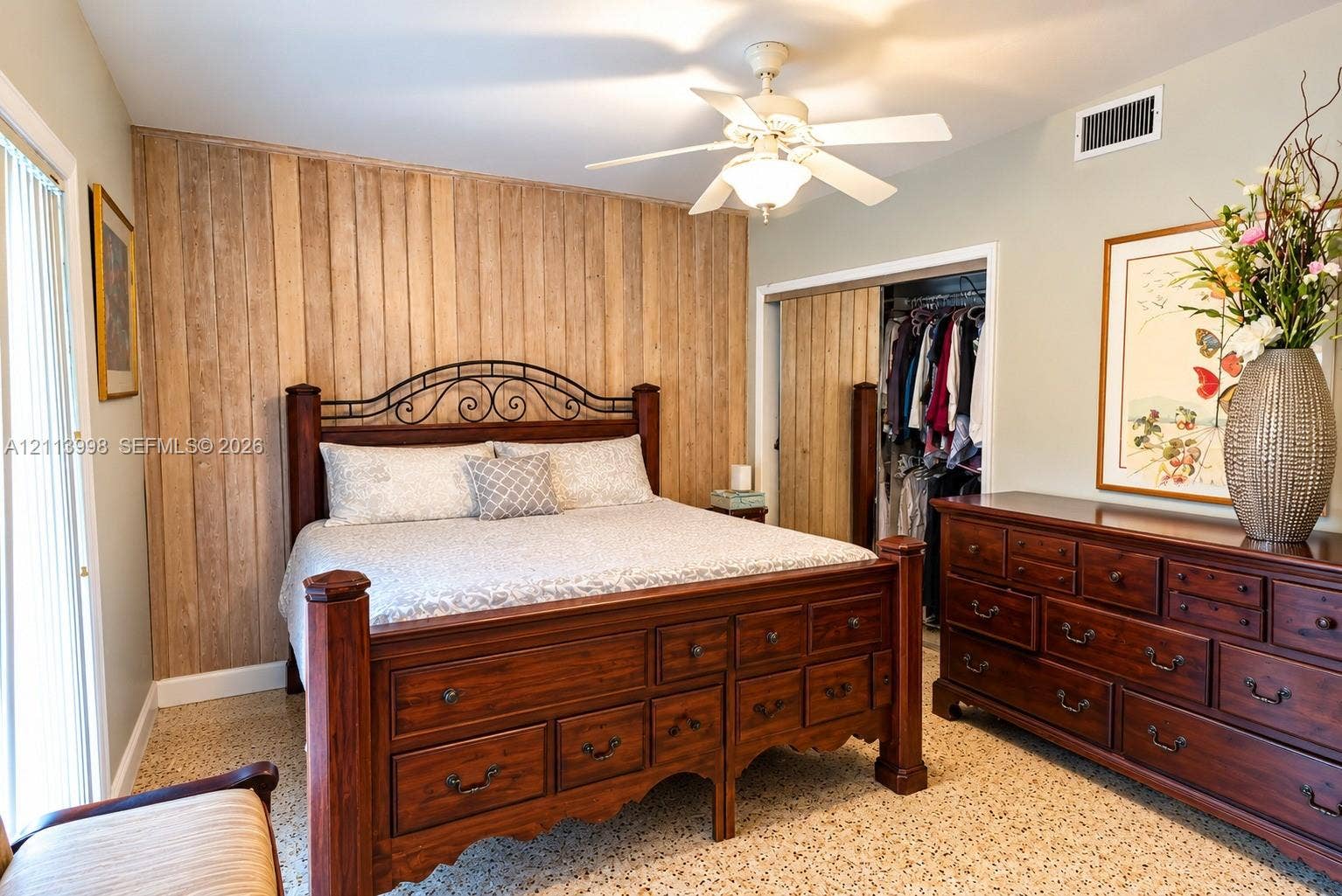 16455 SW 91st Avenue, Palmetto Bay, FL 33157 Vertical wood-plank accent wall, sliding closet doors with matching wood finish, neutral wall paint, overhead ceiling fan with light fixture, and terrazzo flooring