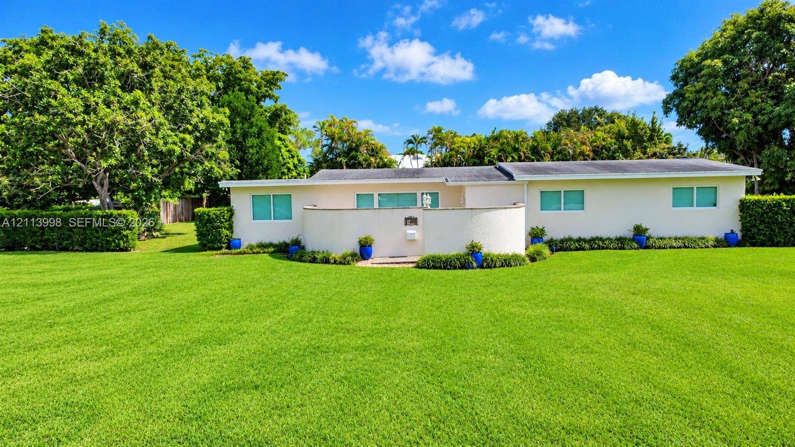 16455 SW 91st Avenue, Palmetto Bay, FL 33157 Single-story exterior featuring a stucco faade, a semi-circular front privacy wall, expansive manicured lawn, and mature perimeter landscaping