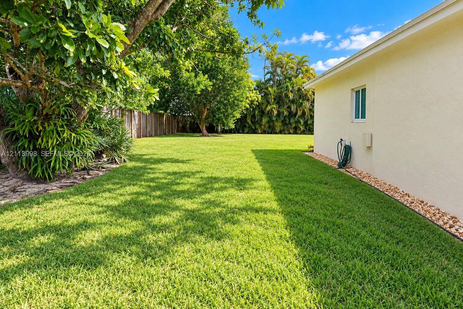 16455 SW 91st Avenue, Palmetto Bay, FL 33157 Expansive grassy side yard featuring mature landscaping, wood-tone fencing, and decorative stone ground cover