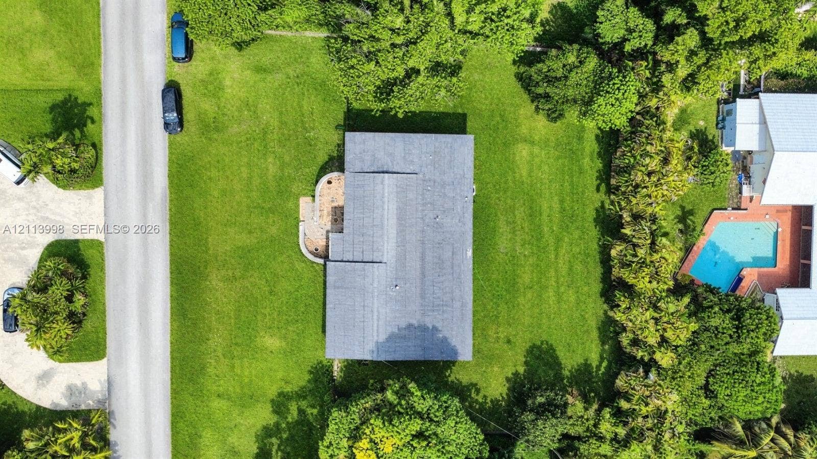 16455 SW 91st Avenue, Palmetto Bay, FL 33157 Aerial perspective featuring a spacious lot with mature perimeter trees, expansive lawn, and a paved walkway