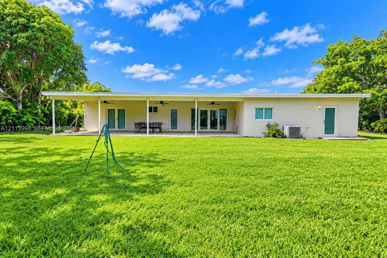16455 SW 91st Avenue, Palmetto Bay, FL 33157 Rear exterior featuring a covered patio, multiple glass-panel doors, ceiling fans, and an expansive lawn
