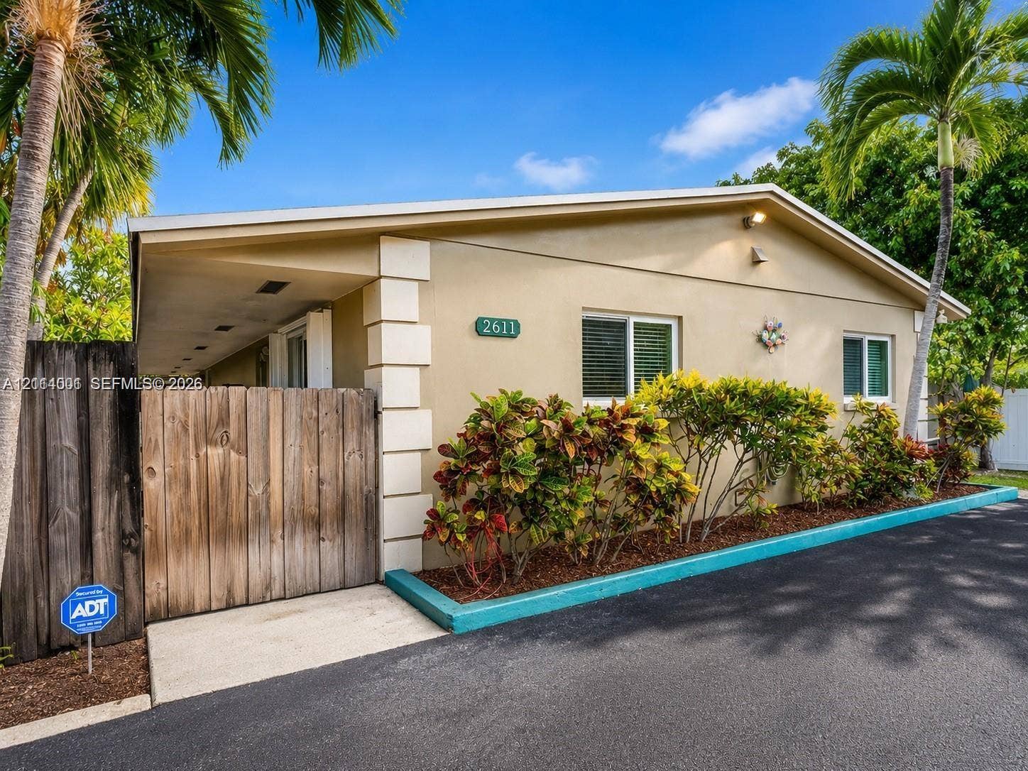 2611 SW 13th Avenue, #1-2, Fort Lauderdale, Fort Lauderdale, FL 33315 Stucco exterior featuring decorative corner quoins, a wood-slat privacy gate, asphalt driveway, and integrated landscaping with mature palm trees
