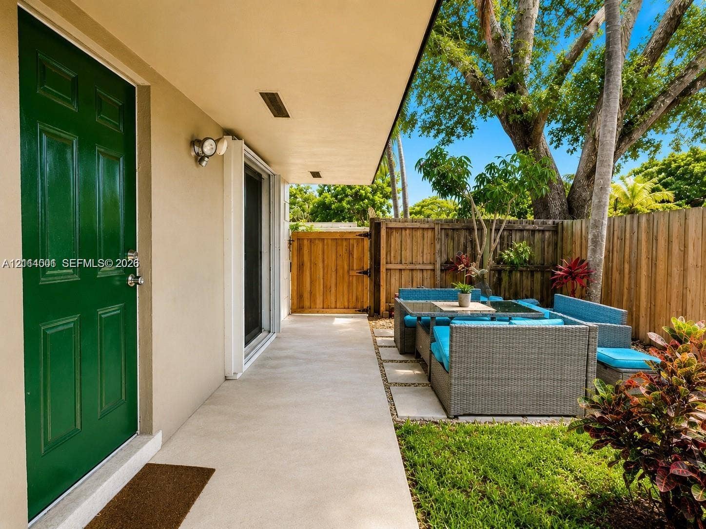 2611 SW 13th Avenue, #1-2, Fort Lauderdale, Fort Lauderdale, FL 33315 Covered concrete patio featuring a solid-color panel door, exterior wall-mounted lighting, and a wood privacy fence