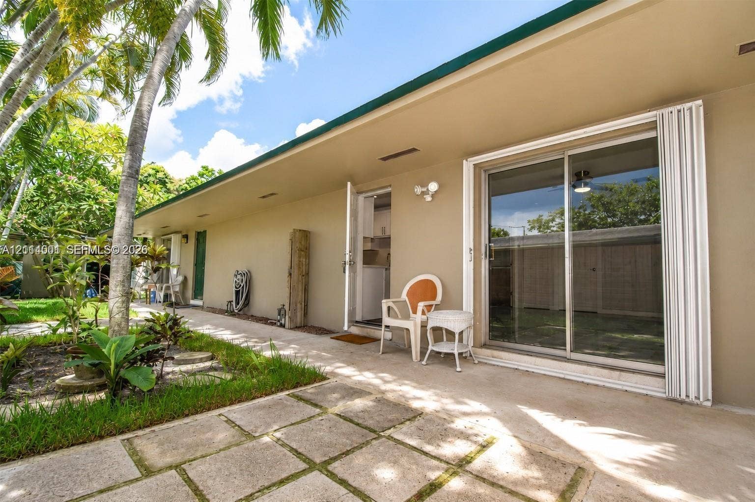 2611 SW 13th Avenue, #1-2, Fort Lauderdale, Fort Lauderdale, FL 33315 Concrete patio with square pavers, exterior sliding glass door, hinged entry door, and perimeter landscaping with palm trees