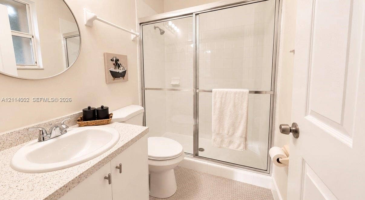 1495 NE 33rd Avenue, #107, Homestead, Homestead, FL 33033 Bathroom featuring a vanity with a stone-composite countertop, oval undermount sink, chrome faucet, circular mirror, and a shower enclosure with sliding glass doors