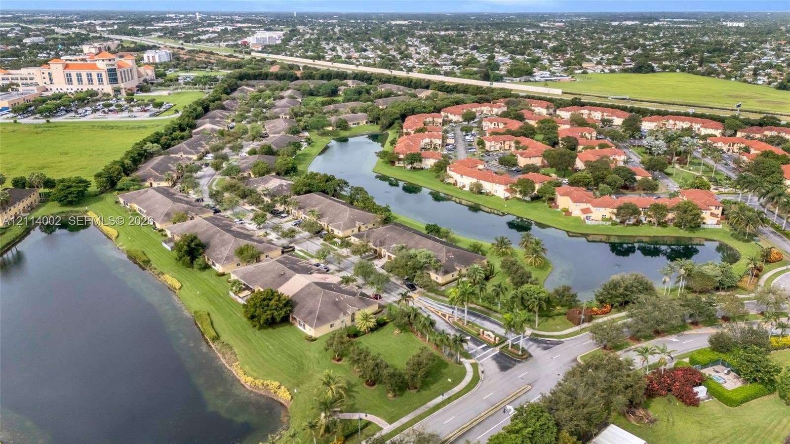 1495 NE 33rd Avenue, #107, Homestead, Homestead, FL 33033 Aerial perspective of a multi-unit residential community featuring terracotta-style roofs, expansive water frontage, paved access roads, and mature perimeter landscaping