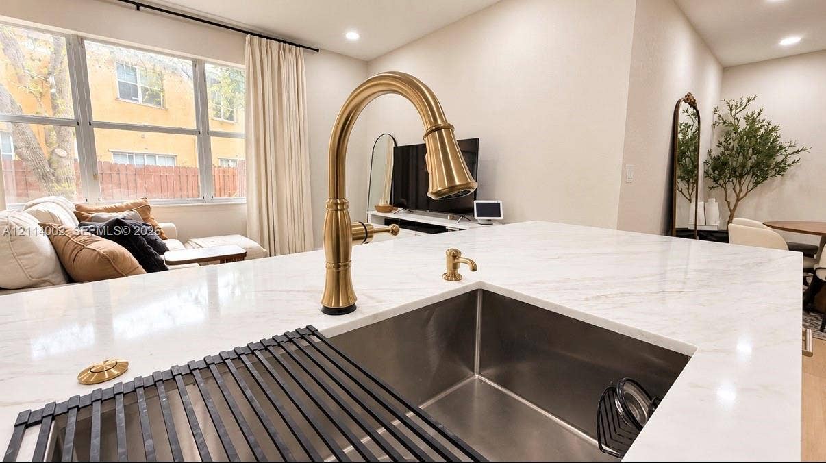 1495 NE 33rd Avenue, #107, Homestead, Homestead, FL 33033 Kitchen island featuring a stone-look countertop, undermount stainless steel sink, and high-arc faucet in a brass finish