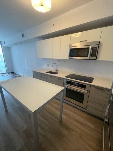 1300 Brickell Bay Drive, #1000, Miami, Miami, FL 33131 Kitchen featuring white flat-panel upper cabinetry, wood-finish lower cabinetry, integrated stainless steel appliances, a stone-surface countertop, and a matching kitchen island