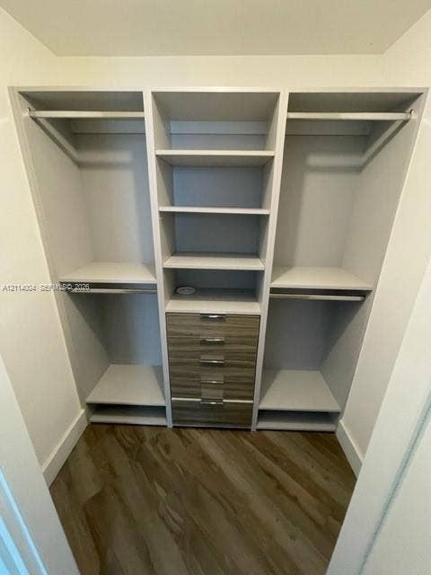 1300 Brickell Bay Drive, #1000, Miami, Miami, FL 33131 Custom built-in closet organization system featuring white shelving, integrated hanging rods, a five-drawer wood-finish cabinet unit with metallic pulls, and wood-finish flooring