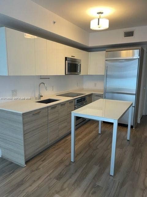 1300 Brickell Bay Drive, #1000, Miami, Miami, FL 33131 Contemporary kitchen featuring glossy upper cabinetry, wood-finish base cabinetry, solid-surface countertops, stainless steel appliances, and wood-finish flooring
