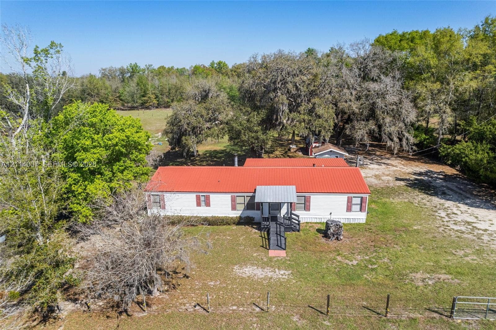 5600 SE 39th Street, Trenton, FL 32693 Single-story residence featuring a red metal roof, white exterior siding, shuttered windows, and a metal entrance ramp