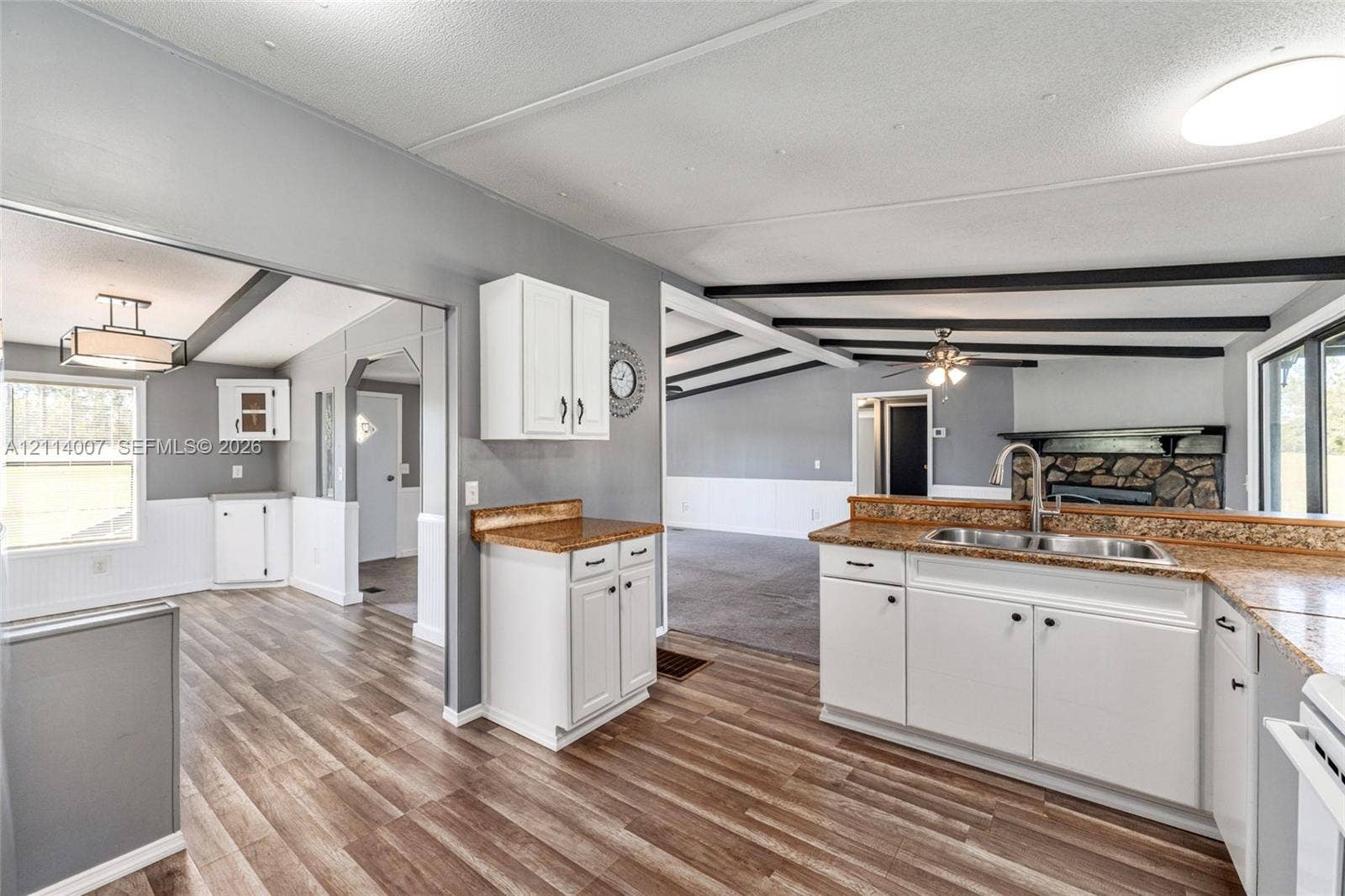 5600 SE 39th Street, Trenton, FL 32693 Kitchen featuring white cabinetry, stone-finish countertops, dual-basin stainless steel sink, wood-finish flooring, and decorative ceiling beams