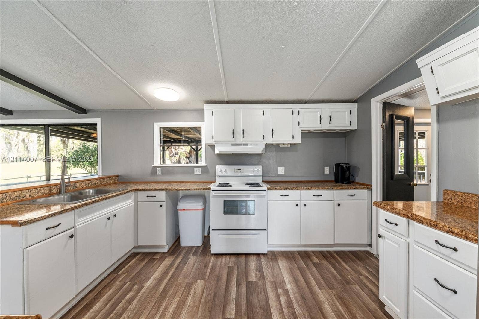 5600 SE 39th Street, Trenton, FL 32693 Kitchen featuring white shaker-style cabinetry, speckled solid-surface countertops, wood-finish flooring, a white freestanding range, and stainless steel dual-basin sink