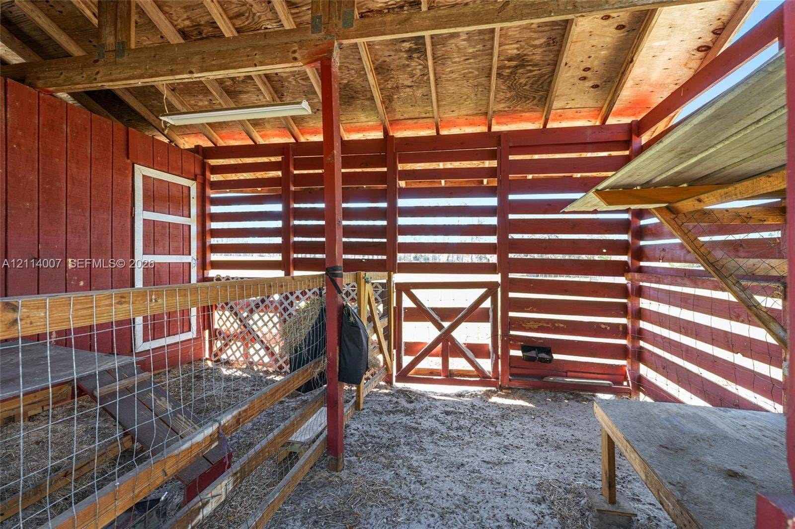 5600 SE 39th Street, Trenton, FL 32693 Open-air structure featuring red-painted horizontal wood siding, exposed rafter ceilings, wood-frame partitions, wire fencing, and an integrated wood-frame gate