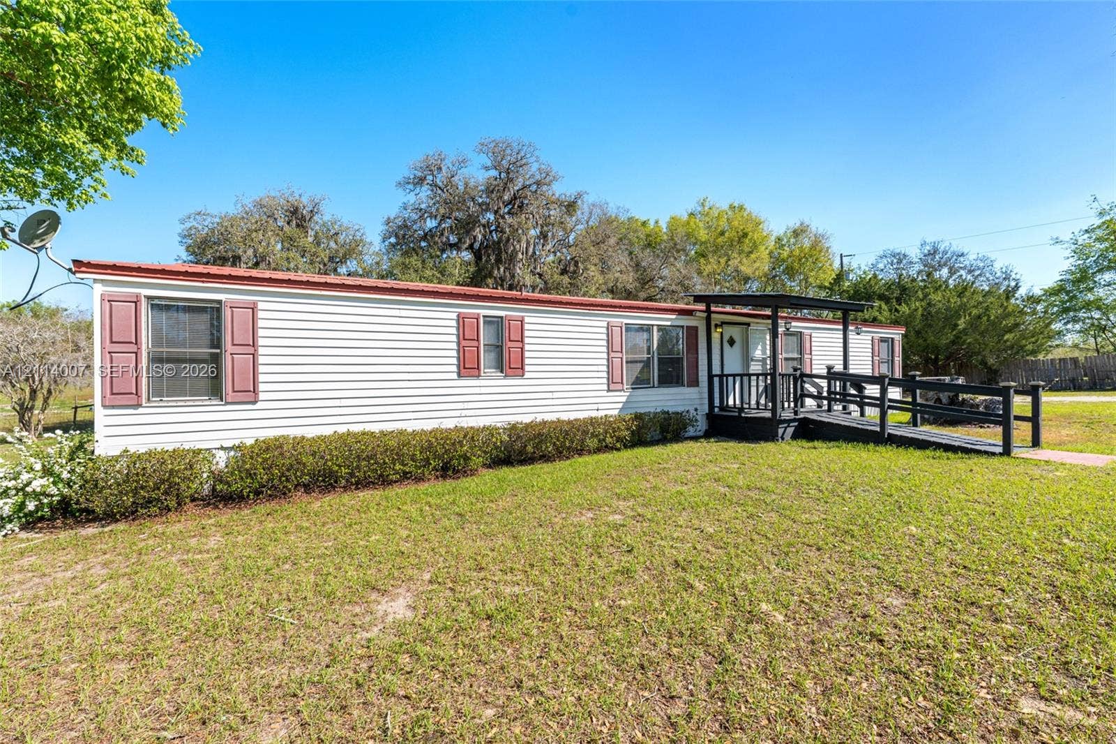 5600 SE 39th Street, Trenton, FL 32693 Exterior featuring light-toned horizontal siding, dark red window shutters, a metal roof, and an elevated entry deck with a wooden ramp