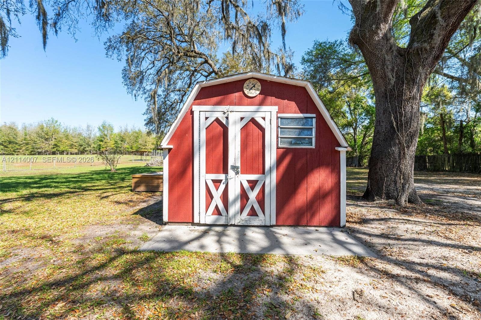 5600 SE 39th Street, Trenton, FL 32693 Gambrel-style outbuilding featuring red wood-finish siding, white trim, double entry doors, and a horizontal louvered window set on a concrete foundation