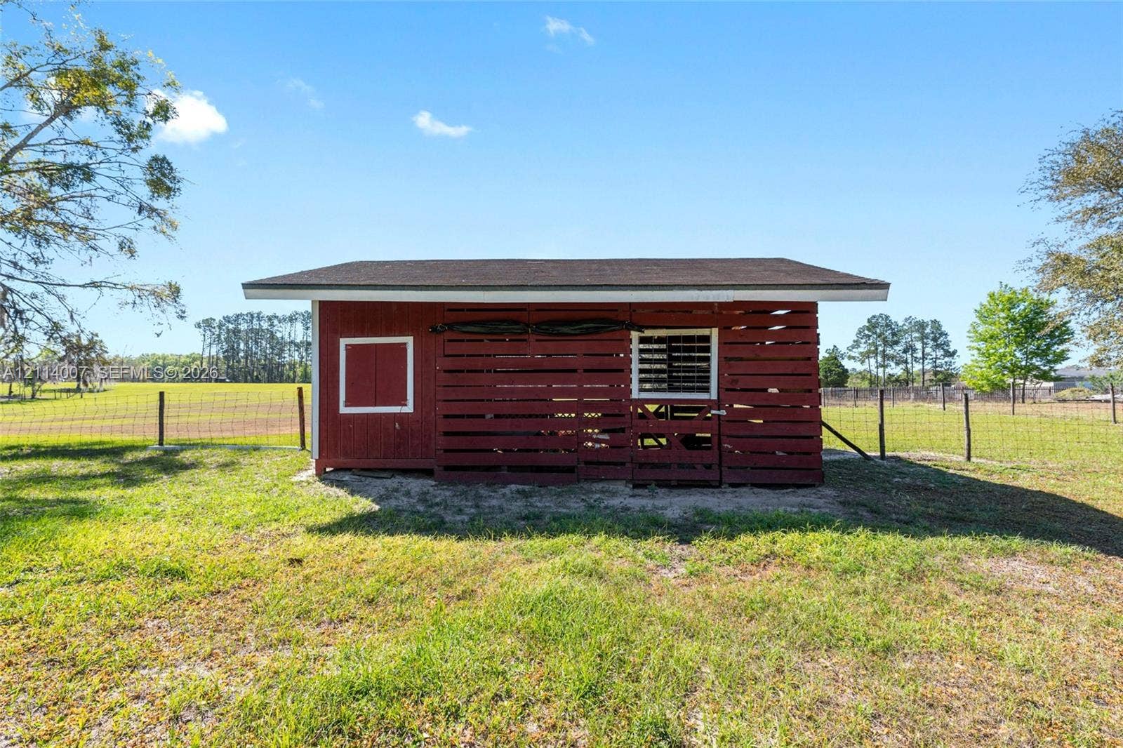 5600 SE 39th Street, Trenton, FL 32693 Red wooden outbuilding featuring horizontal slat siding, a pitched roof, and wire-fenced perimeter grounds