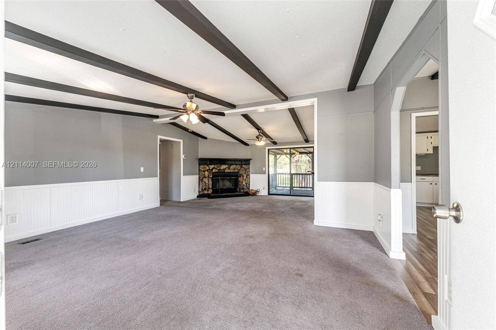 5600 SE 39th Street, Trenton, FL 32693 Living area featuring decorative ceiling beams, stone-surround fireplace, dual ceiling fans, and wainscoting
