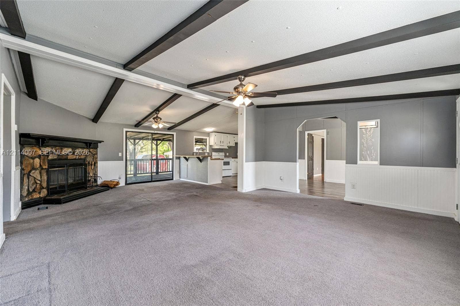 5600 SE 39th Street, Trenton, FL 32693 Vaulted ceiling featuring exposed dark beams, floor-to-ceiling stone fireplace, beadboard wainscoting, sliding glass door, and dual ceiling fans