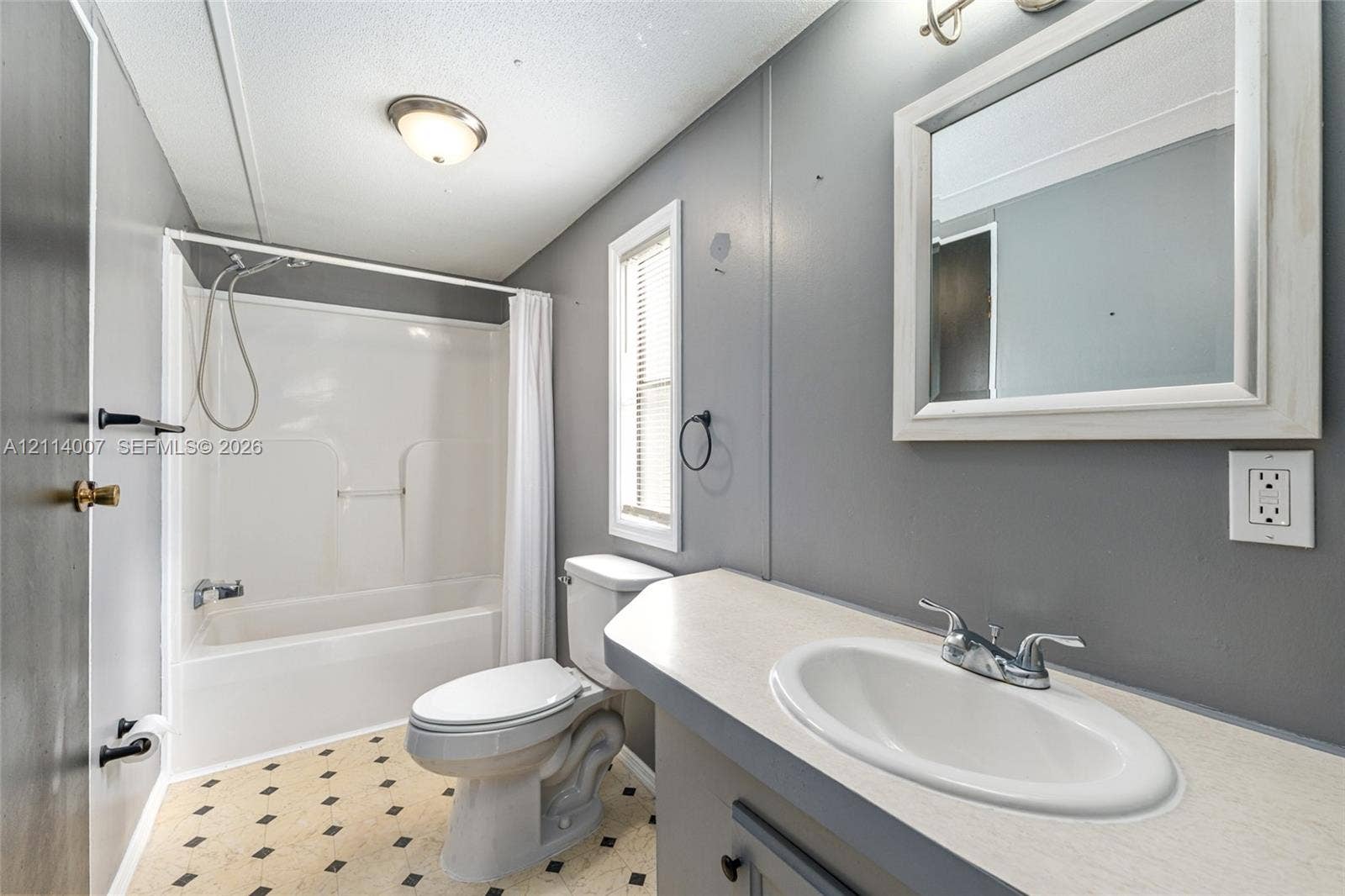 5600 SE 39th Street, Trenton, FL 32693 Bathroom featuring a vanity with a drop-in sink, a wall-mounted mirror with a frame, a tub and shower combination with a hand-held sprayer, and patterned flooring