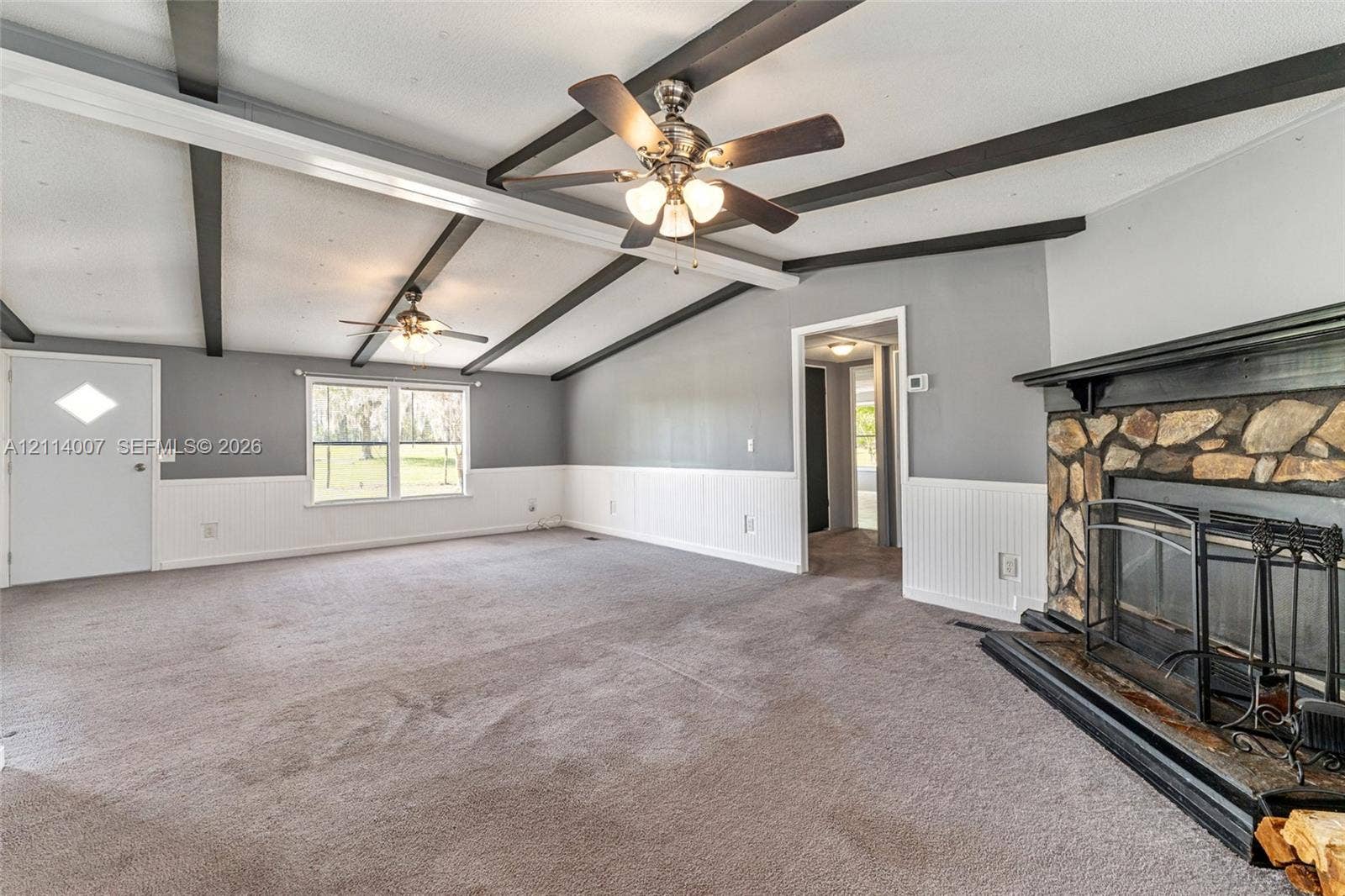 5600 SE 39th Street, Trenton, FL 32693 Vaulted ceiling with exposed decorative beams, stone-faced fireplace with a mantel, white wainscoting, and dual ceiling fans