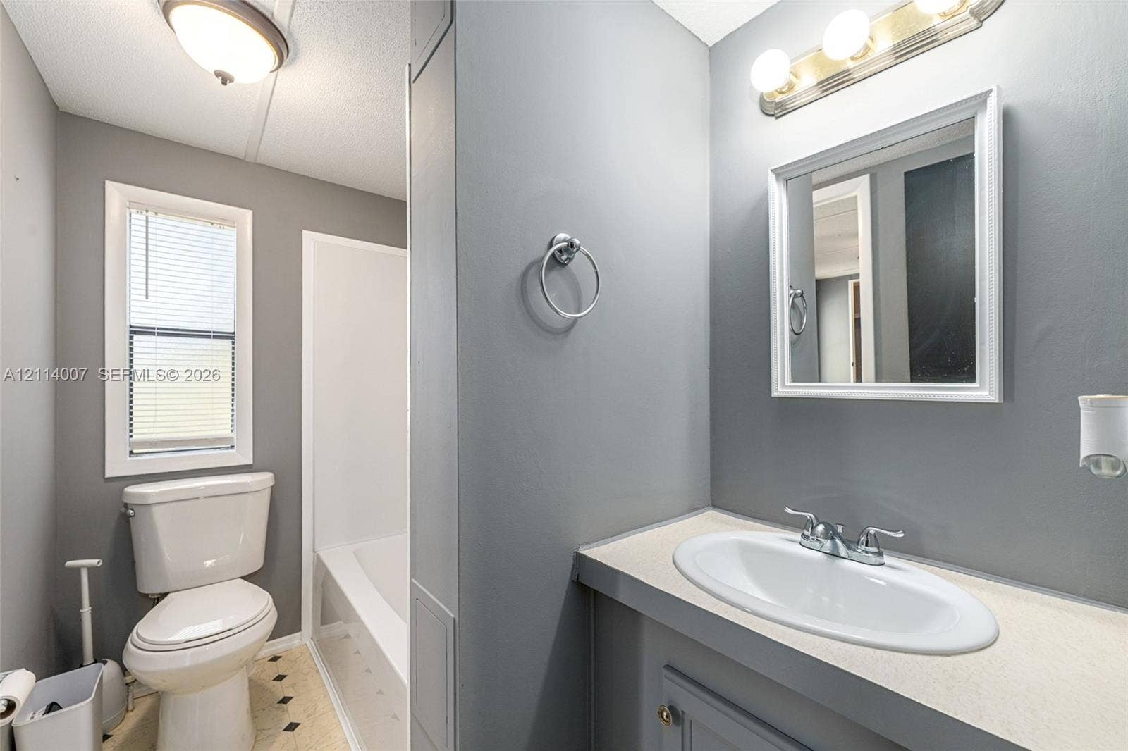 5600 SE 39th Street, Trenton, FL 32693 Bathroom featuring a vanity with a white integrated oval sink, a wall-mounted three-light fixture, a framed mirror, a separate tub-shower combination, and a window