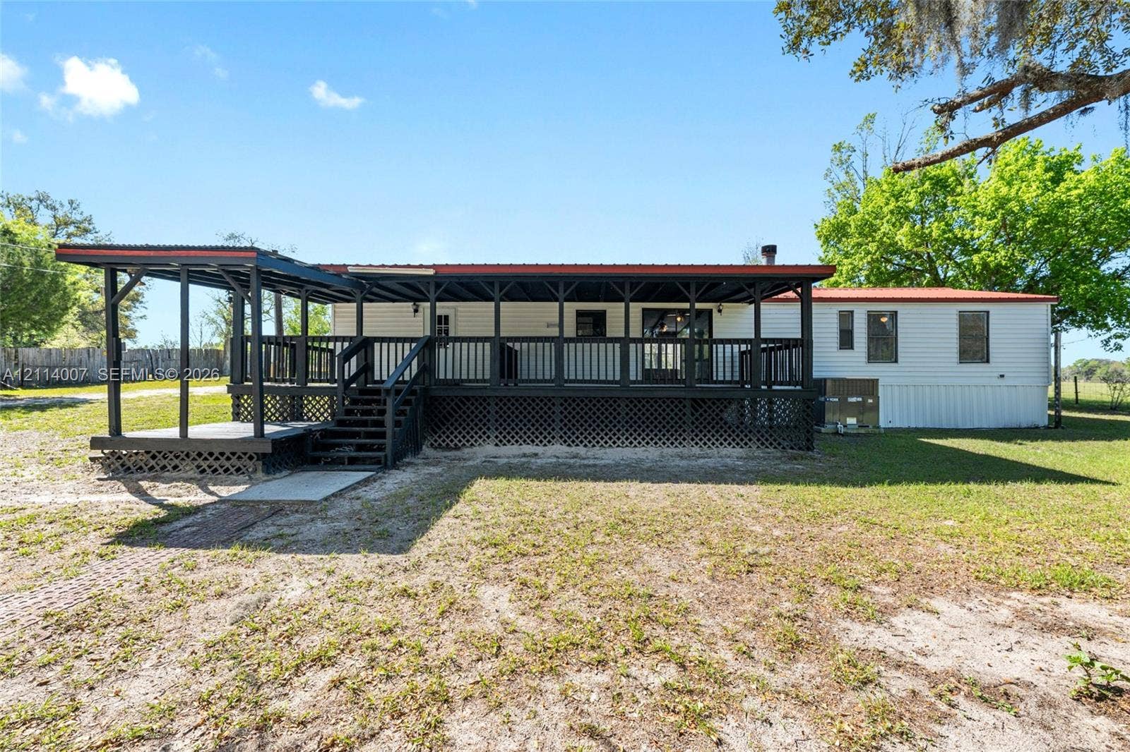 5600 SE 39th Street, Trenton, FL 32693 Exterior featuring a sprawling covered deck with dark wooden railings, a metal roof, and lattice skirting