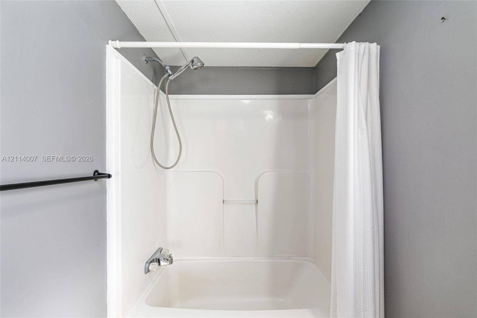 5600 SE 39th Street, Trenton, FL 32693 Bathtub with an integrated white surround, wall-mounted hand-held shower fixture, and a built-in recessed shelf