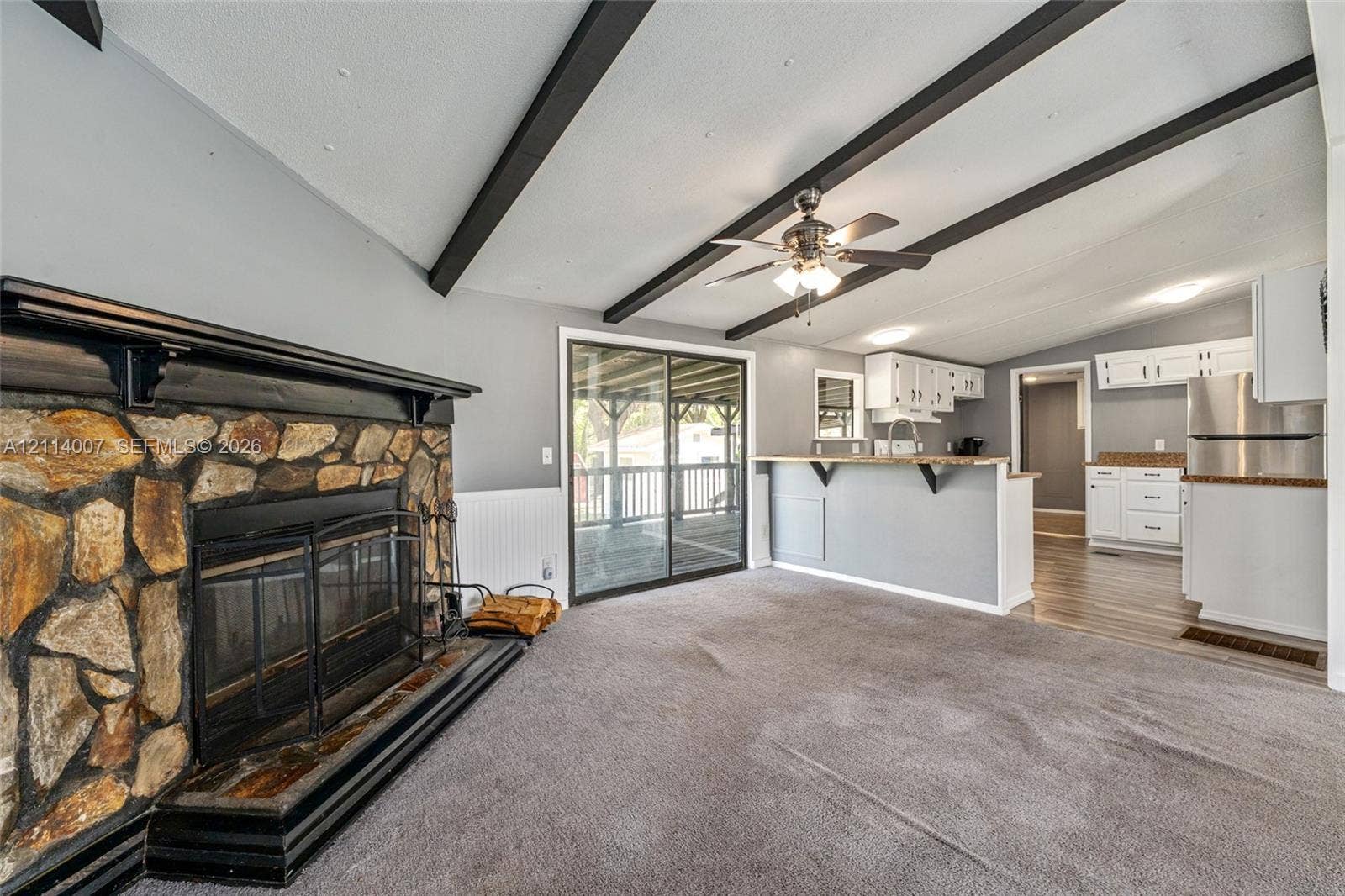 5600 SE 39th Street, Trenton, FL 32693 Vaulted ceiling featuring exposed dark beams, stone-faced fireplace with a black mantel, kitchen peninsula with overhead cabinetry, and sliding glass doors