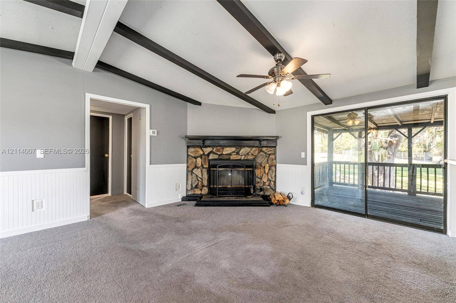 5600 SE 39th Street, Trenton, FL 32693 Living area featuring vaulted ceilings with decorative exposed beams, stone-surround fireplace with a wooden mantel, white wainscoting, and sliding glass doors