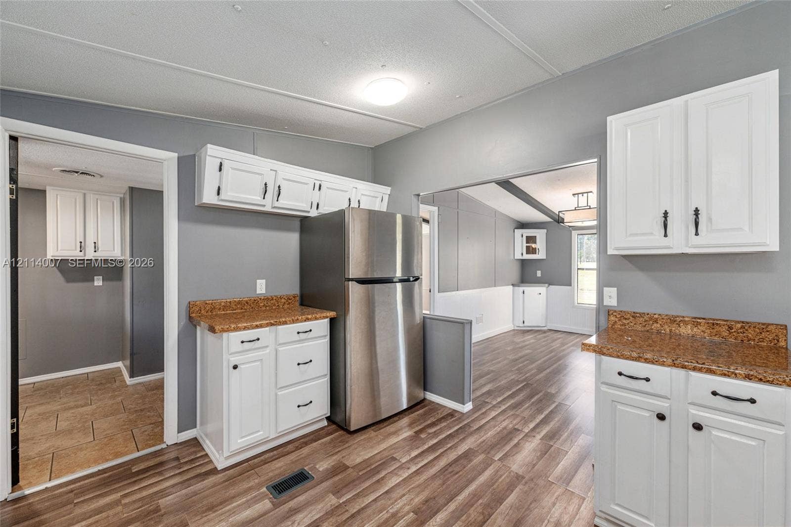 5600 SE 39th Street, Trenton, FL 32693 Kitchen featuring white cabinetry, speckled stone-finish countertops, stainless steel refrigerator, and wood-finish flooring