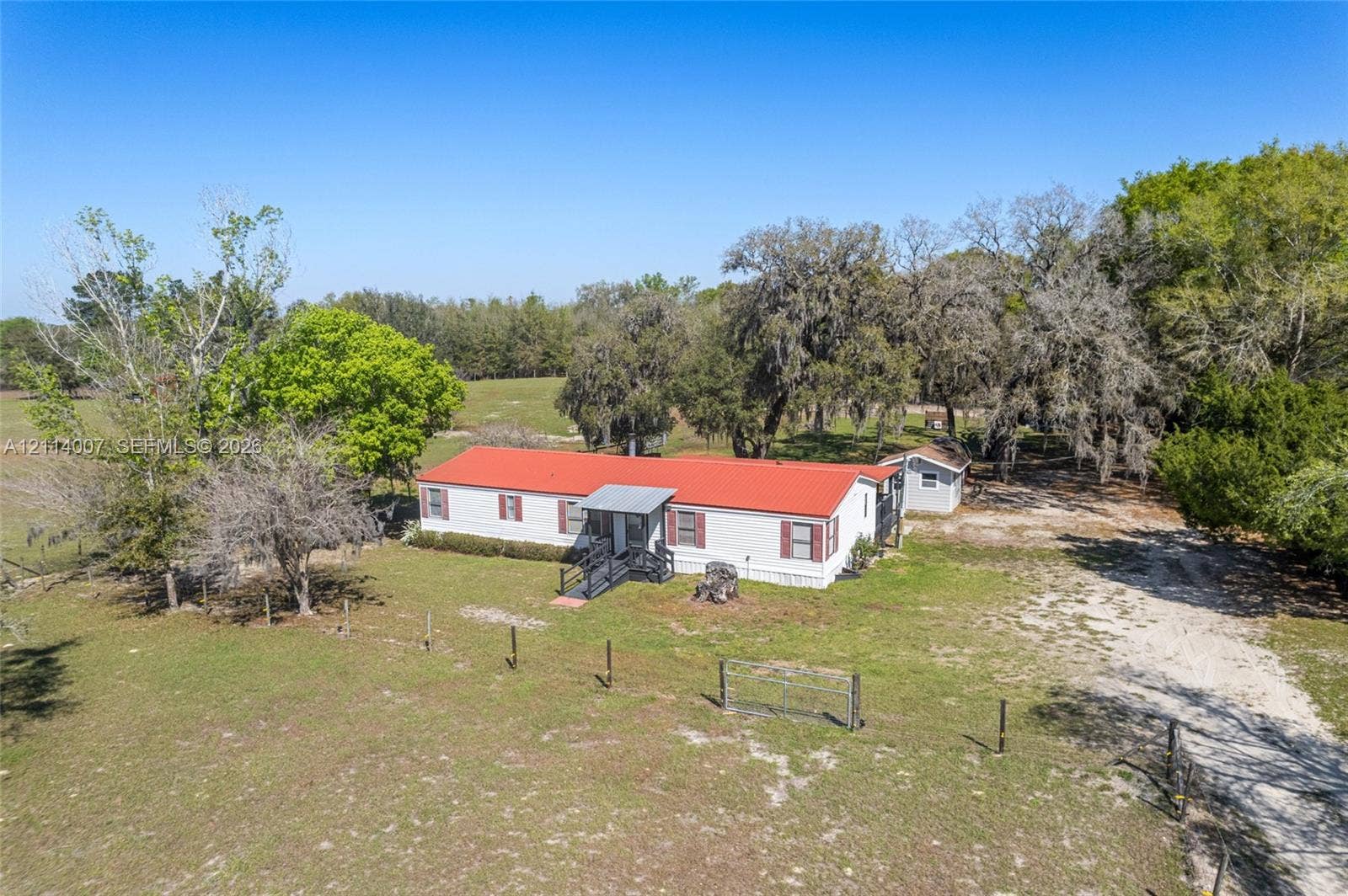 5600 SE 39th Street, Trenton, FL 32693 Single-story exterior featuring a metal roof, light-toned siding, dark window shutters, metal railed entryway, and expansive surrounding acreage with mature trees