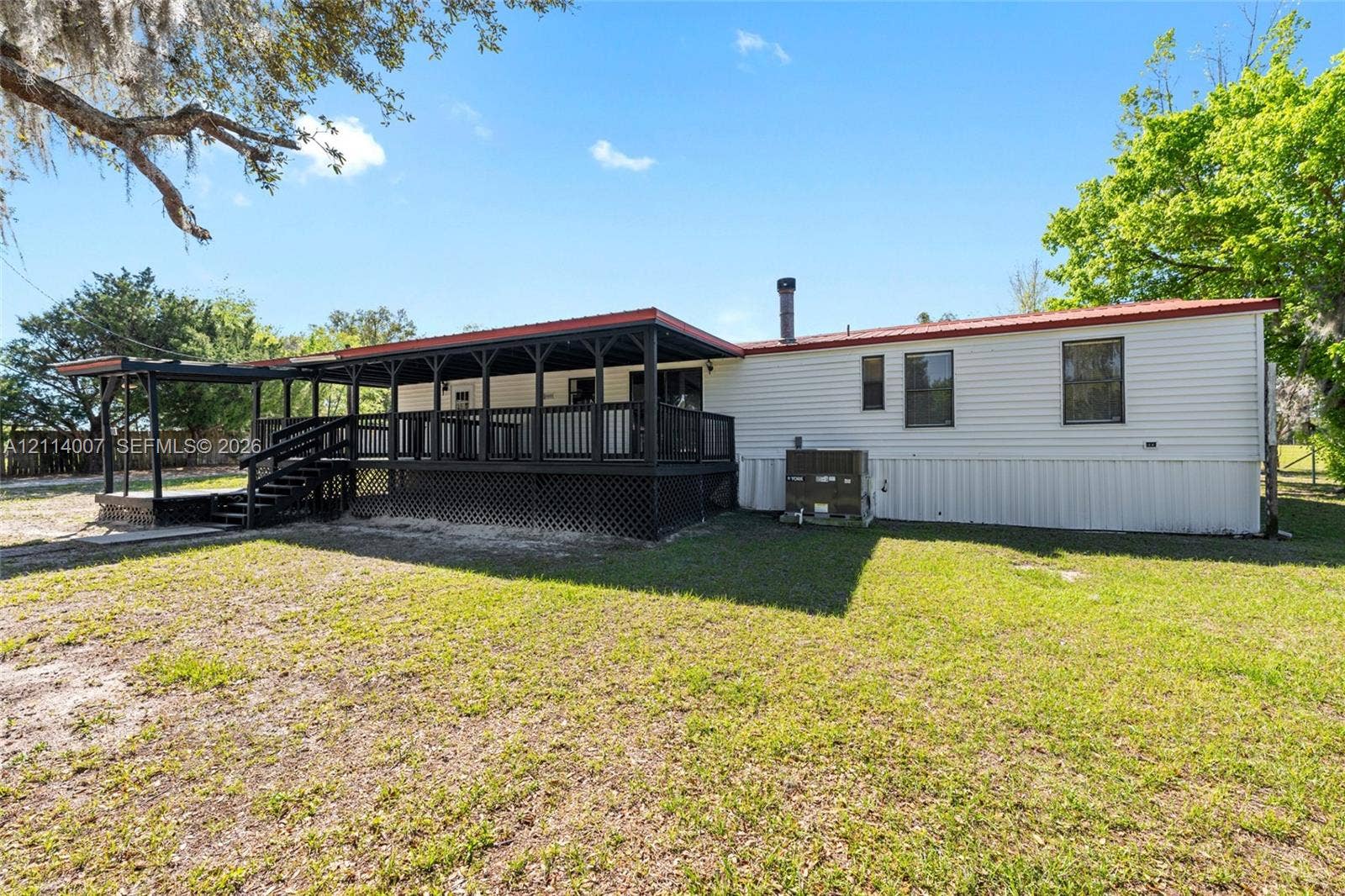 5600 SE 39th Street, Trenton, FL 32693 Exterior featuring horizontal siding, a covered wraparound wood deck with lattice skirting, and a metal roof