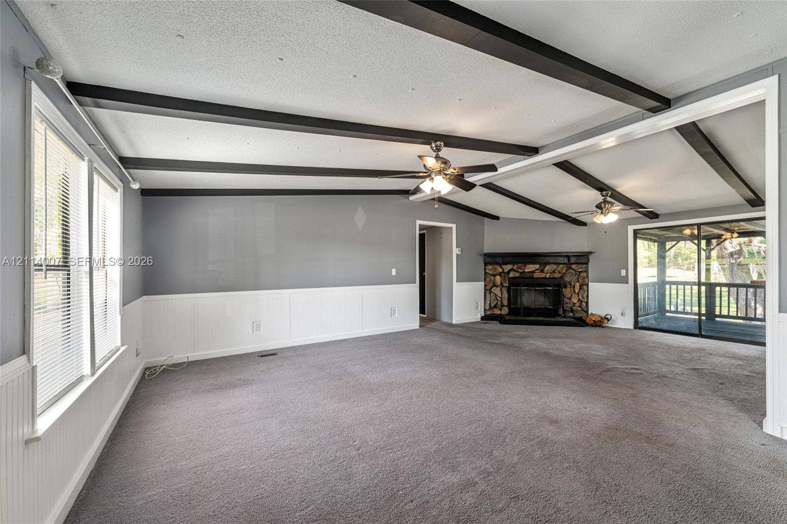 5600 SE 39th Street, Trenton, FL 32693 Living area featuring exposed ceiling beams, a stone-surround fireplace, wainscoting, and dual ceiling fans