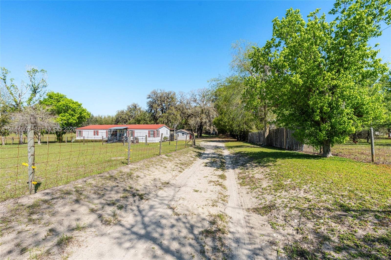 5600 SE 39th Street, Trenton, FL 32693 Single-level dwelling with a red metal roof, gravel driveway, wire fencing, and mature trees on a sprawling lot