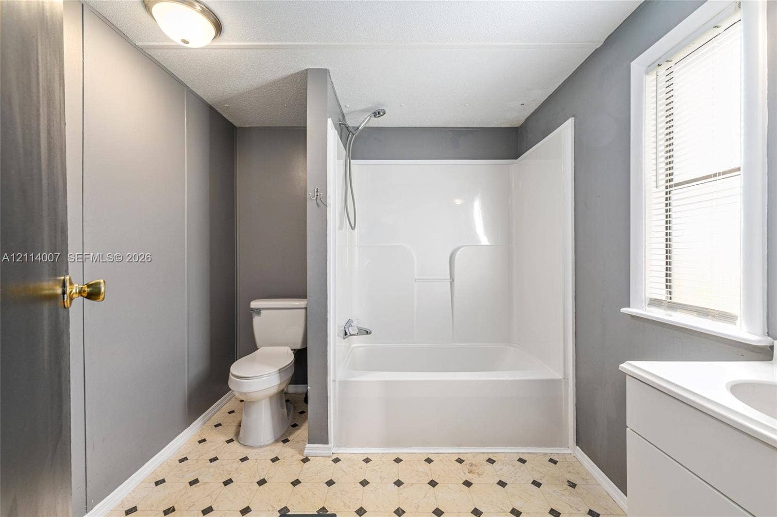 5600 SE 39th Street, Trenton, FL 32693 Bathroom featuring a white tub-shower combination, pedestal toilet, white vanity with an integrated sink, window with horizontal blinds, and patterned tile flooring