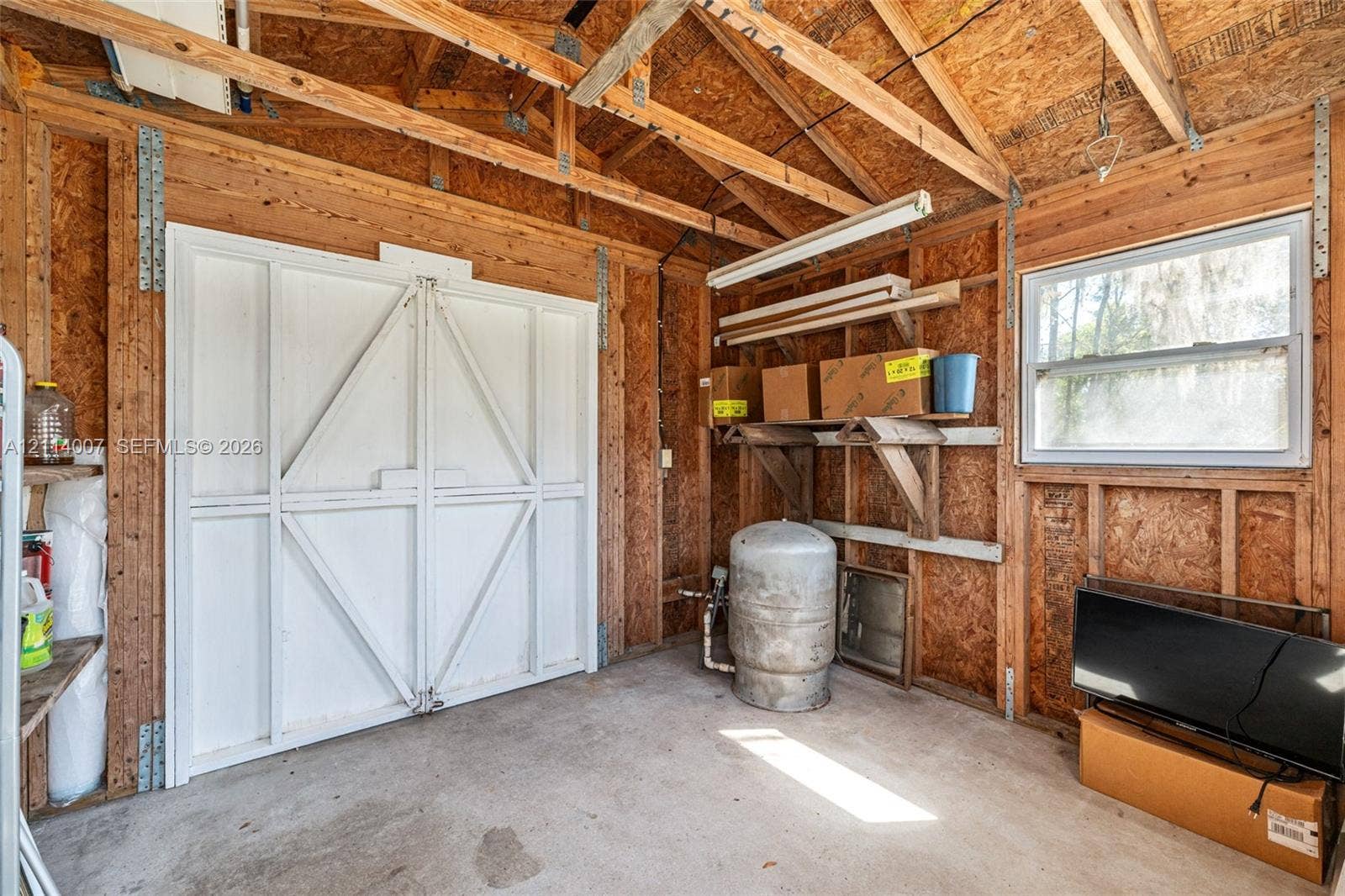 5600 SE 39th Street, Trenton, FL 32693 Utility shed featuring exposed wood-stud construction, concrete flooring, double-door entry, and a single-pane window