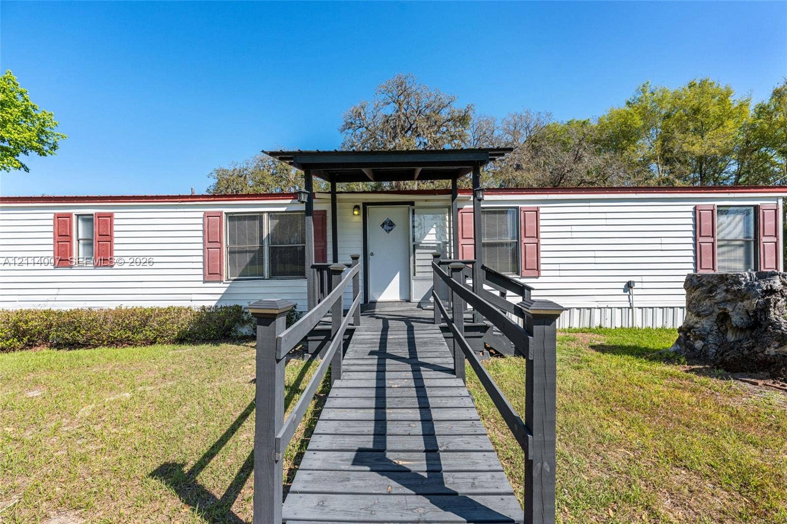 5600 SE 39th Street, Trenton, FL 32693 Exterior featuring white horizontal siding, dark-toned shutters, a covered front entryway, and a wooden accessibility ramp with handrails