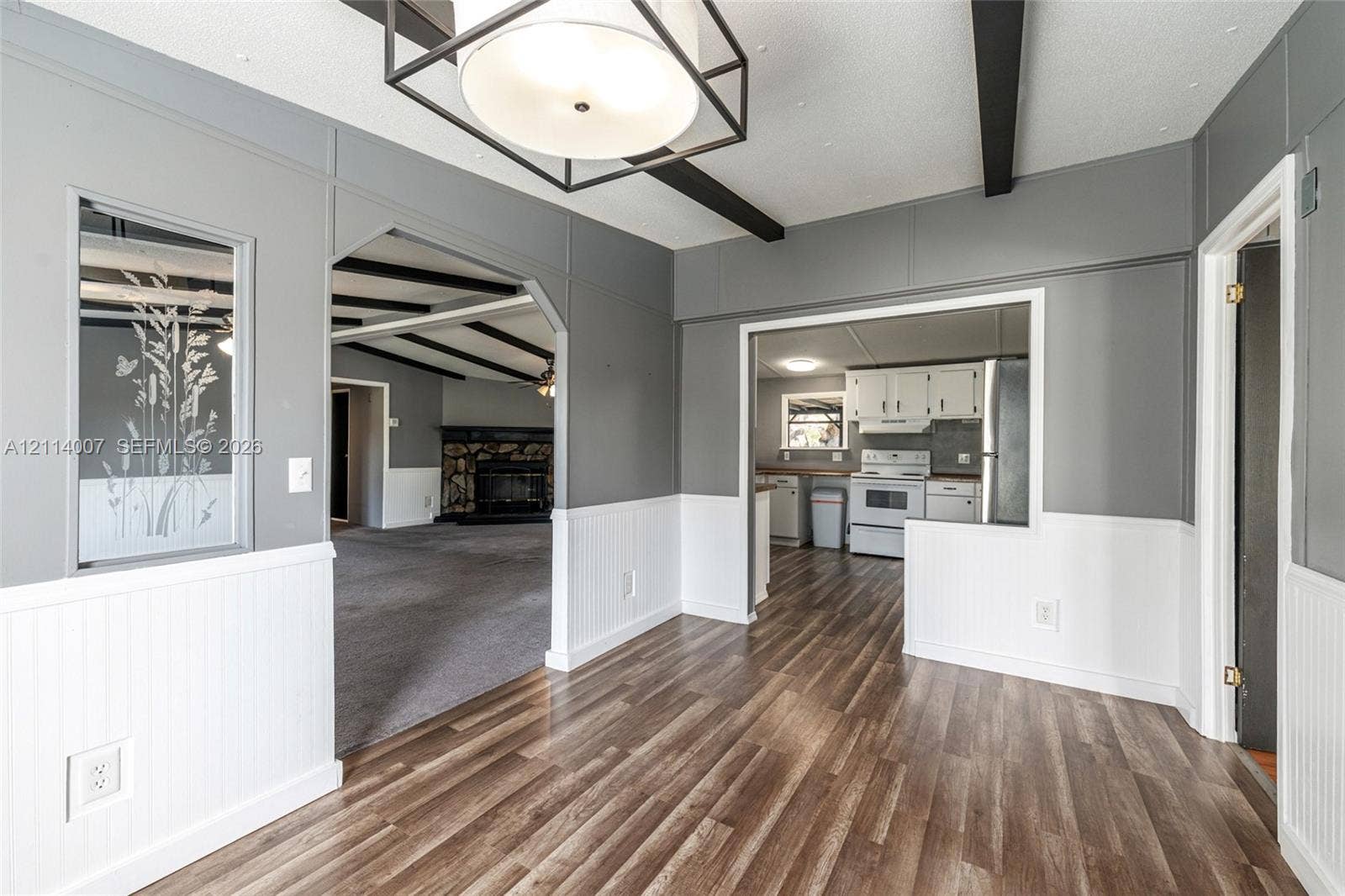 5600 SE 39th Street, Trenton, FL 32693 Dining area featuring wood-finish flooring, beadboard wainscoting, a geometric lantern-style pendant light fixture, and dark exposed ceiling beams