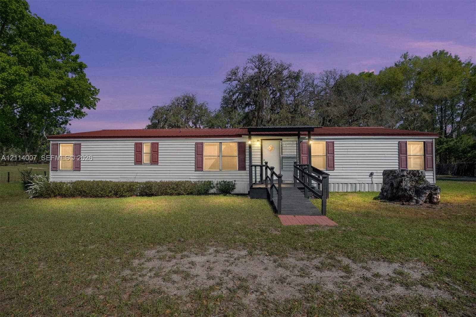 5600 SE 39th Street, Trenton, FL 32693 Single-story exterior featuring light-colored horizontal siding, dark-toned shutters, a metal roof, and an elevated entry landing with a staircase and railing