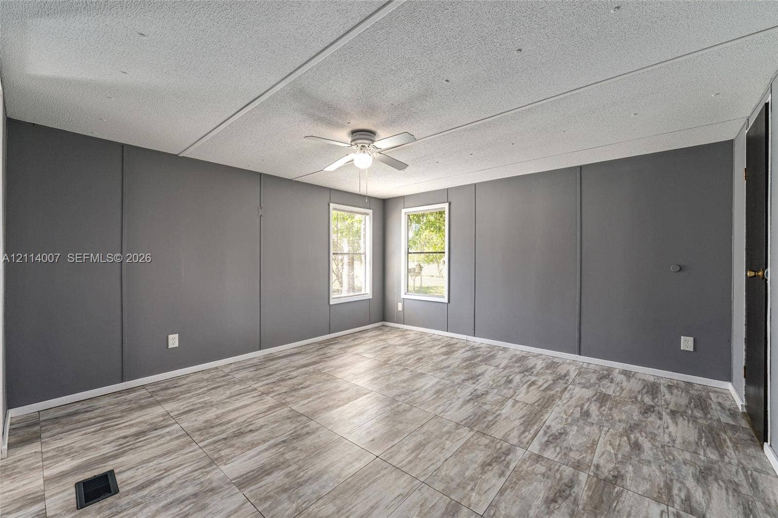 5600 SE 39th Street, Trenton, FL 32693 Room featuring wood-finish tile flooring, painted gray panel walls, two double-hung windows, and a central ceiling fan