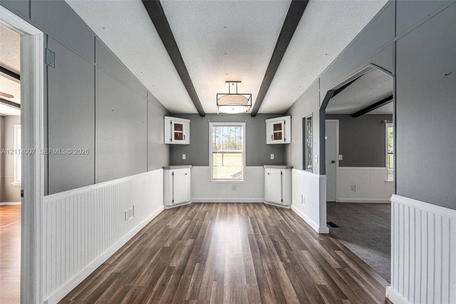 5600 SE 39th Street, Trenton, FL 32693 Interior space featuring wood-finish flooring, beadboard wainscoting, built-in corner cabinetry, exposed ceiling beams, and a drum-style pendant light fixture