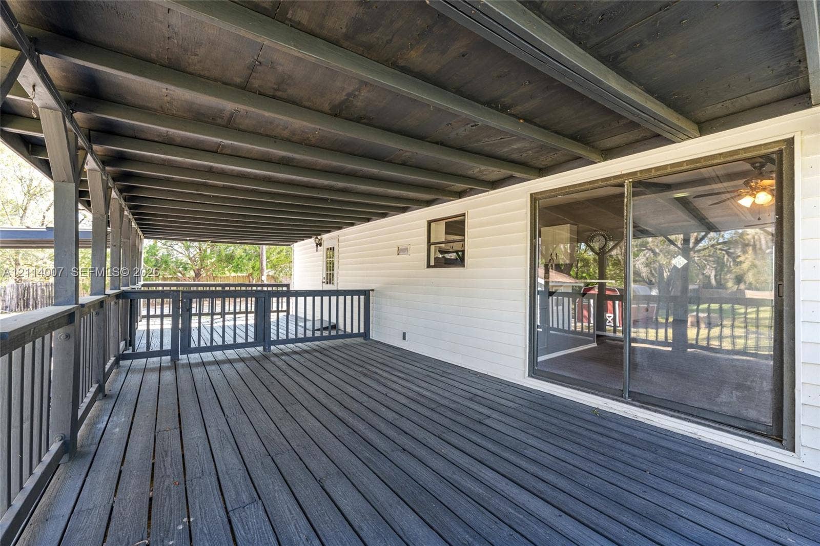 5600 SE 39th Street, Trenton, FL 32693 Covered wooden deck featuring dark-stained plank flooring, an overhead beam structure, perimeter railing with a gated entrance, and a sliding glass door