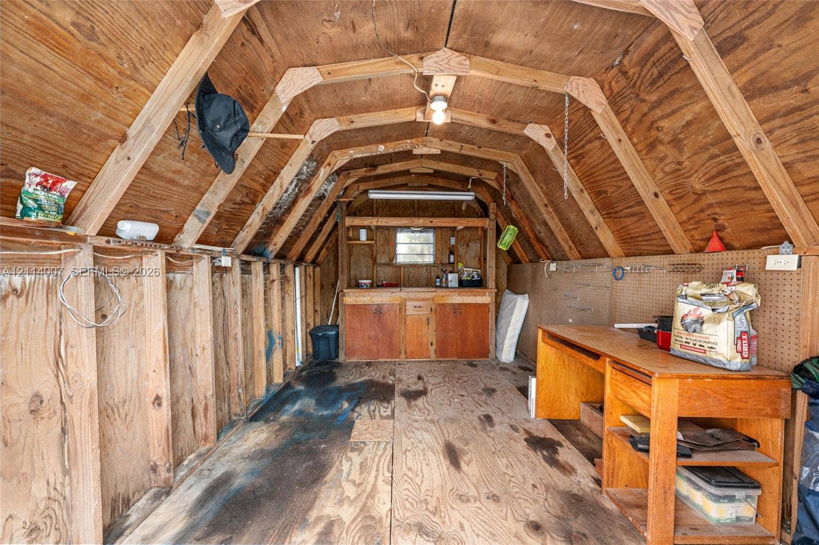 5600 SE 39th Street, Trenton, FL 32693 Detached storage structure featuring exposed wood framing, plywood wall paneling, built-in wooden cabinetry, integrated workbench, and overhead lighting