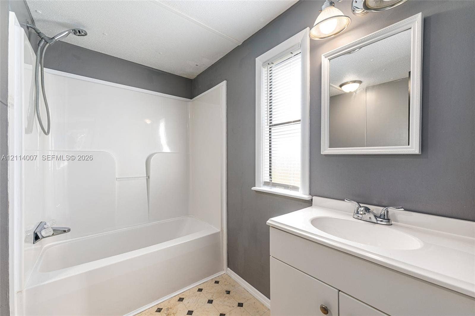5600 SE 39th Street, Trenton, FL 32693 Bathroom featuring a white tub-shower combination, a vanity with a white integrated sink, a wall-mounted mirror, and patterned tile flooring