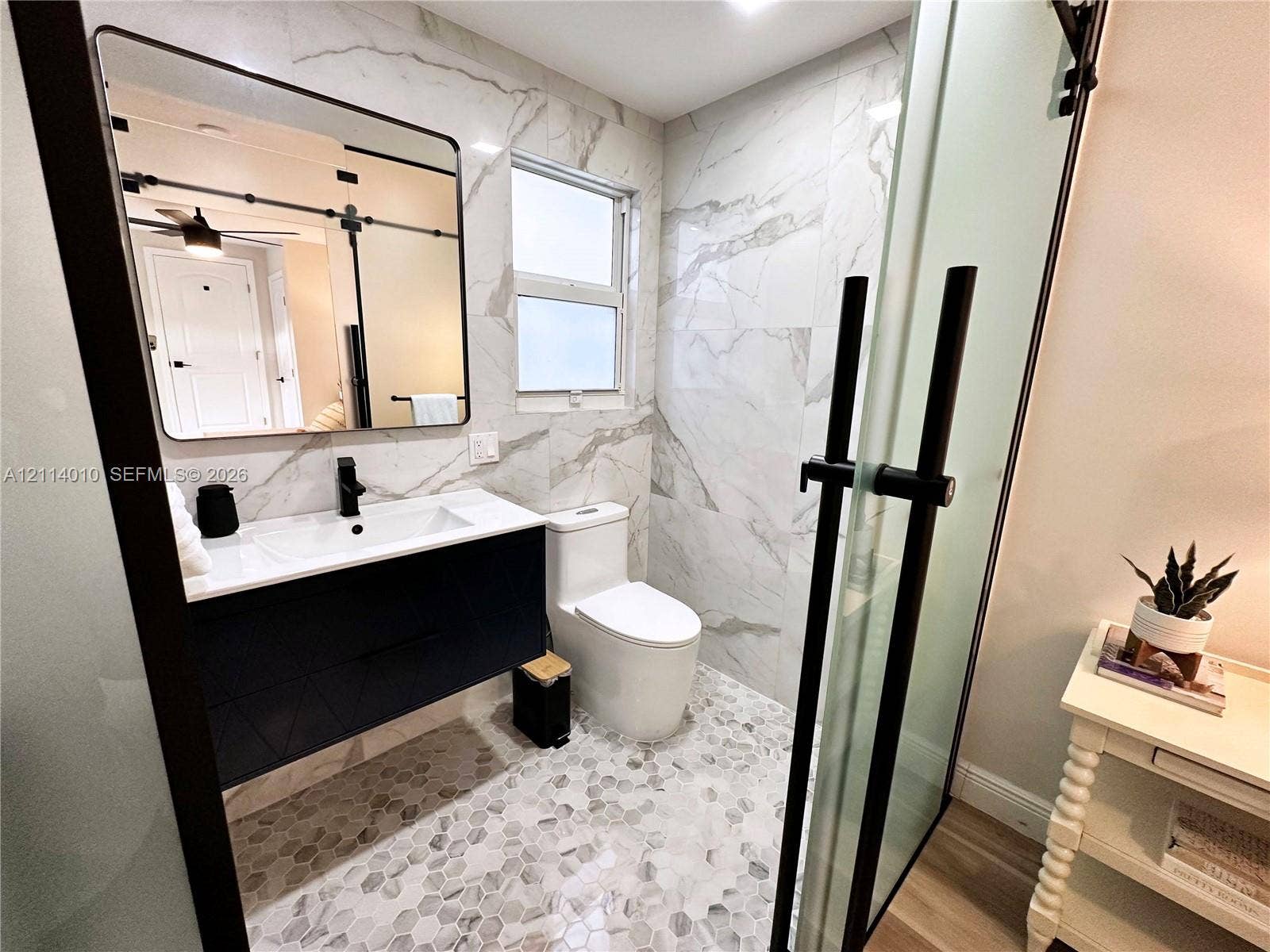 1161-1163 SW 30th Street, Fort Lauderdale, FL 33315 Floating vanity with a white countertop and dark cabinetry, rectangular under-mount sink with a matte black faucet, wall-mounted mirror with a black frame, full-height wall tile with stone-patterned veining, and hexagonal tile flooring